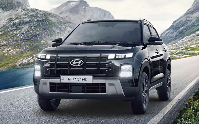 A black Hyundai SUV driving on a scenic mountain road with lush green hills and rocky mountains in the background.